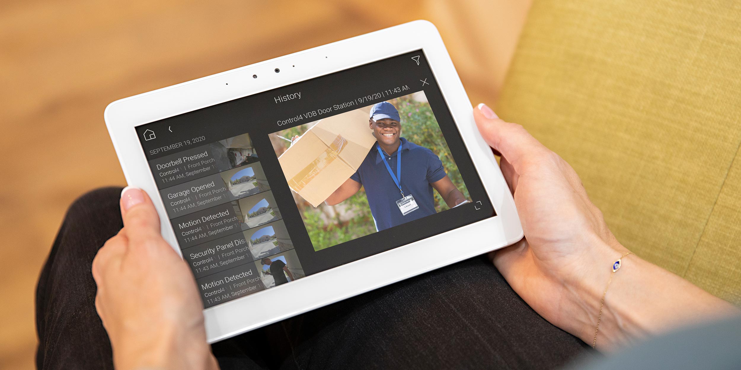 A person holding a tablet displaying a security camera feed of a package delivery.