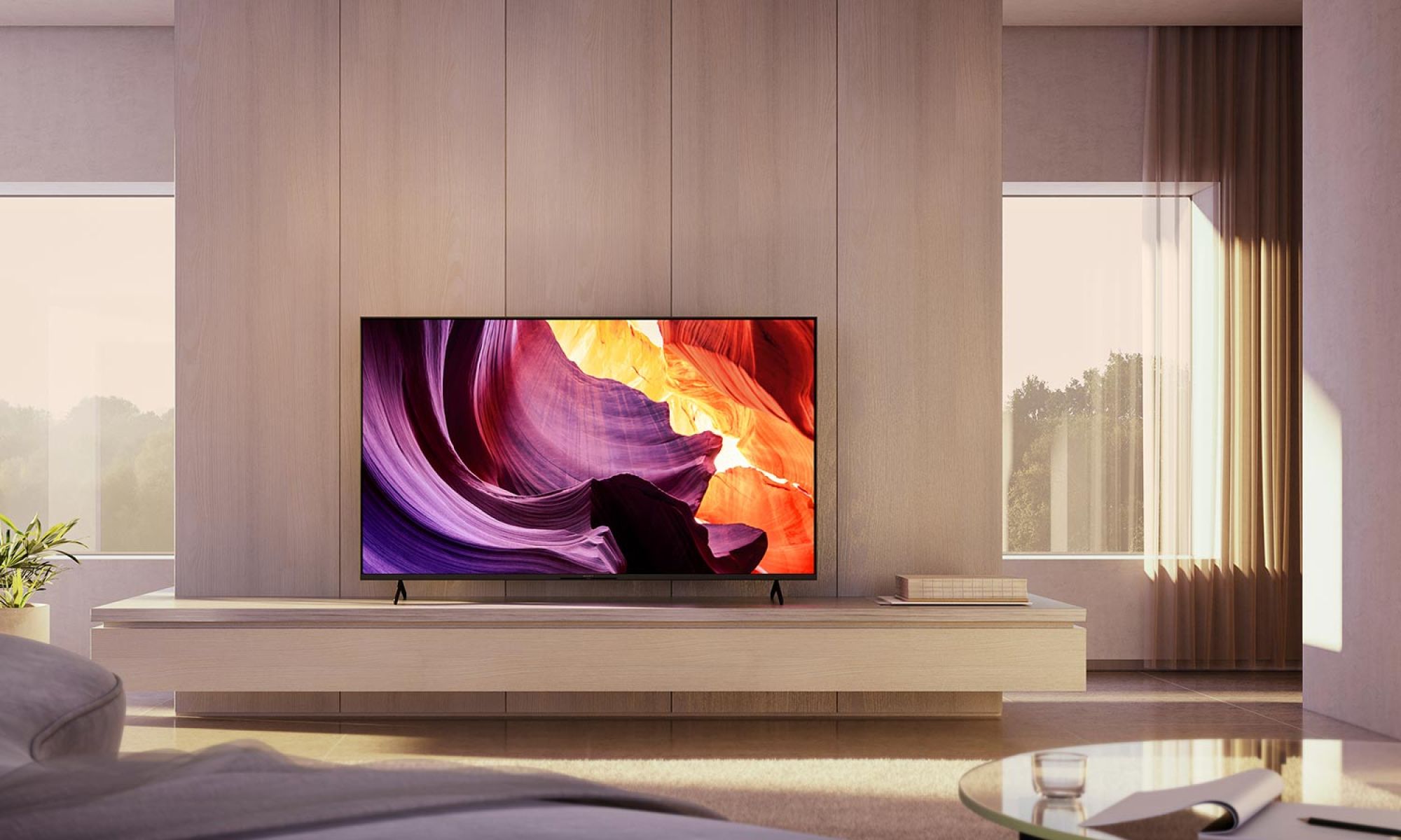 A minimalist living space with a large flat-screen TV on a wood-paneled wall, streaming vibrant abstract visuals. Floor-to-ceiling windows with sheer curtains let in soft natural light.